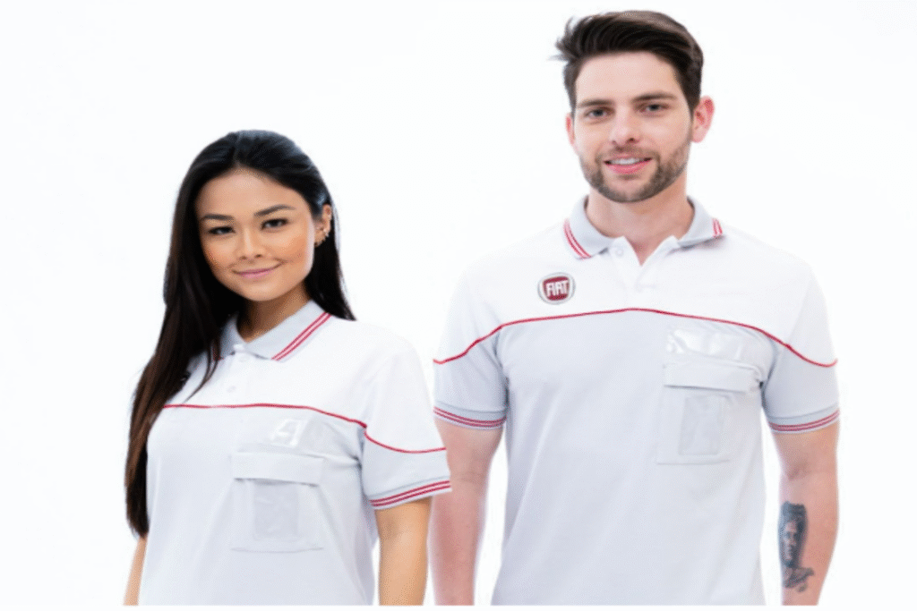 Dois profissionais utilizando roupas de proteção e capacetes brancos analisam um painel elétrico, enquanto um deles aponta para o equipamento e o outro segura um tablet.