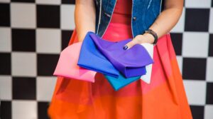 Pessoa segura amostras de tecidos coloridos, incluindo tons vibrantes como vermelho, laranja e azul-claro, sobre uma mesa branca.