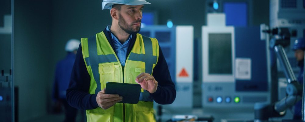 Engenheiro com capacete branco e colete refletivo operando tablet em fábrica